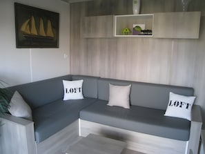 A grey sectional sofa with two pillows, one with 'LOFT' text, and a small shelf above with decorative items.