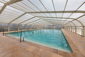 Une piscine intérieure dotée d’un toit en verre et de rampes en métal.