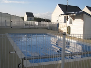 A swimming pool with a metal fence, surrounded by buildings with white siding and dark roofs.