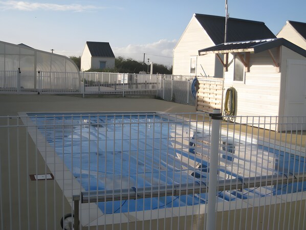 A swimming pool with a metal fence, surrounded by buildings with white siding and dark roofs.