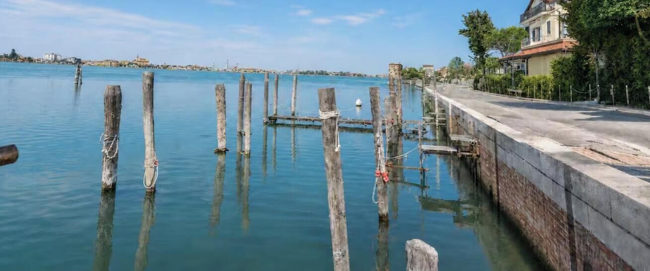 A waterfront property with a concrete dock, wooden posts, and a building with a red roof.