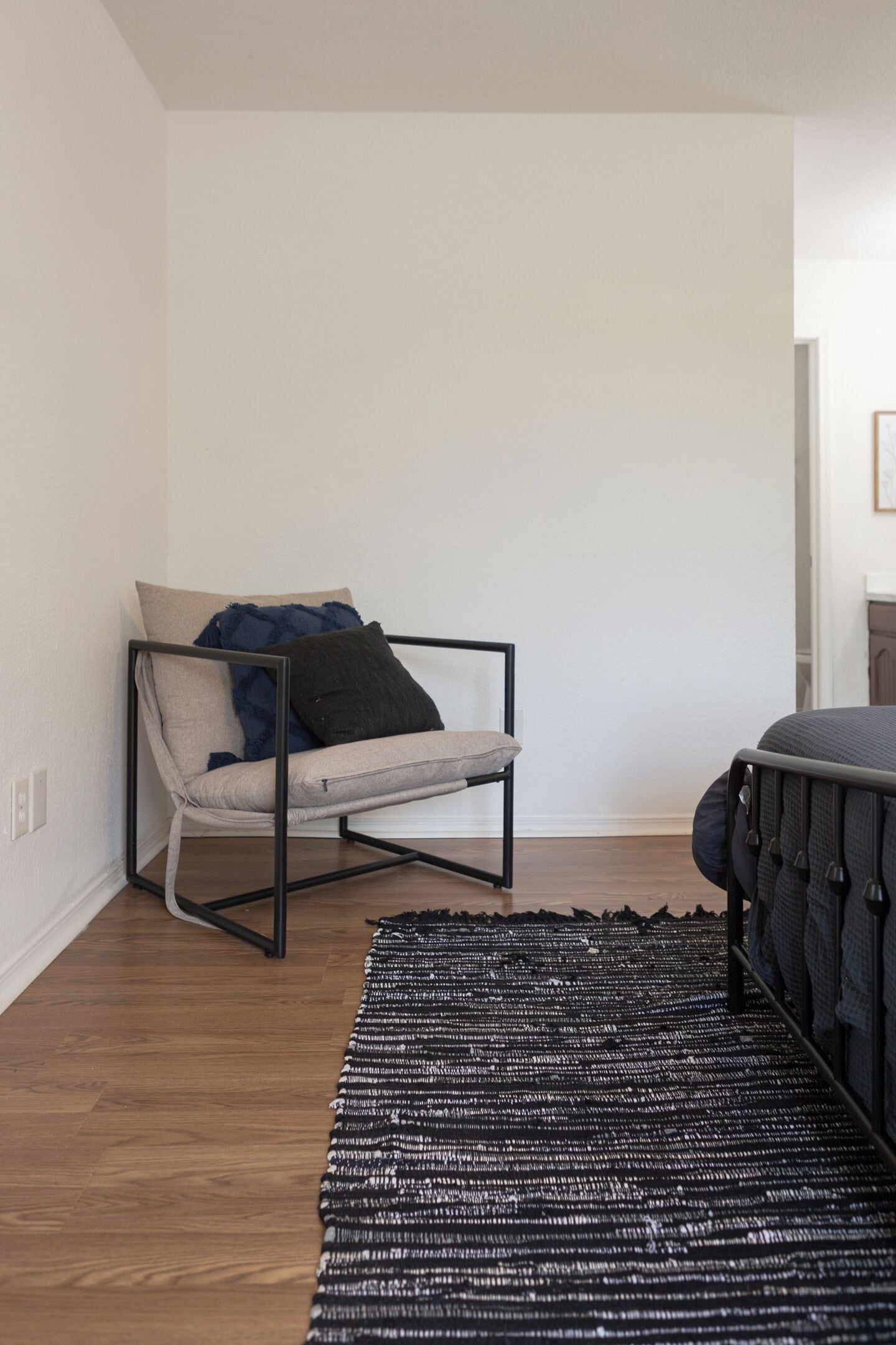 Ein Zimmer mit einem Sessel, einem Bett, einem schwarz-weißen Teppich und einer weißen Wand.