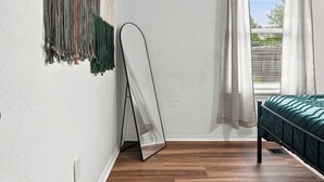 Una stanza con un letto, una sedia a dondolo, una finestra con tende e un arazzo appeso al muro.
