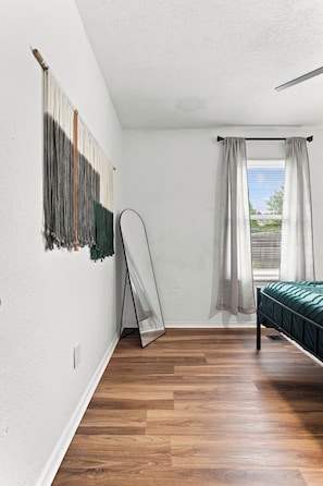A room with a bed, a hanging chair, a window with curtains, and a wall-mounted tapestry. - The Grove on 66th- 3B 2Bth Tulsa Duplex (Tulsa)