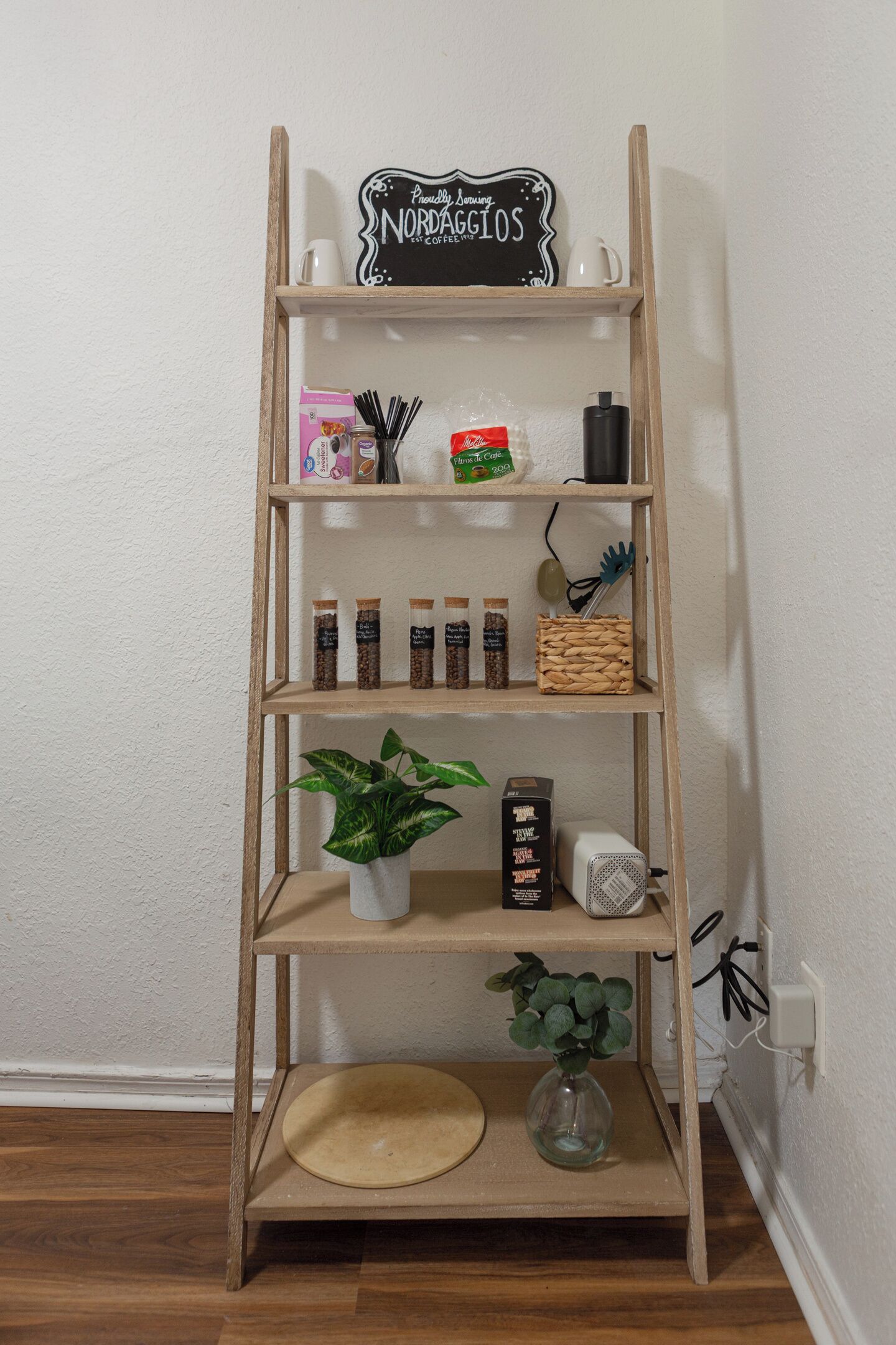 Estante de madeira com diversos objetos, incluindo uma placa, potes, uma planta e um pequeno alto-falante.