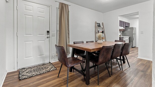 Una zona pranzo con tavolo e sedie in legno, una porta bianca e una cucina sullo sfondo.