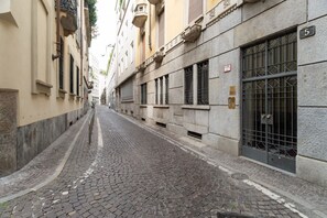 A narrow cobblestone street flanked by historic buildings with barred windows and a number plaque. - Spacious 200 sqm apartment, ideal for groups of up to 8 people, located on the 2nd floor of a building with an elevator.The property is centrally located, just a 7-minute walk from the San Babila M1 metro stop and a 14-minute walk from the Duomo.Essent (Milan)