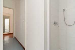 A bathroom with white tiles, a shower with a handheld hose, and a visible door leading to another room. - Spacious 200 sqm apartment, ideal for groups of up to 8 people, located on the 2nd floor of a building with an elevator.The property is centrally located, just a 7-minute walk from the San Babila M1 metro stop and a 14-minute walk from the Duomo.Essent (Milan)