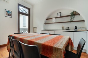 A dining area with a table set for four, a kitchen with white cabinets, and a window with blinds. - Spacious 200 sqm apartment, ideal for groups of up to 8 people, located on the 2nd floor of a building with an elevator.The property is centrally located, just a 7-minute walk from the San Babila M1 metro stop and a 14-minute walk from the Duomo.Essent (Milan)
