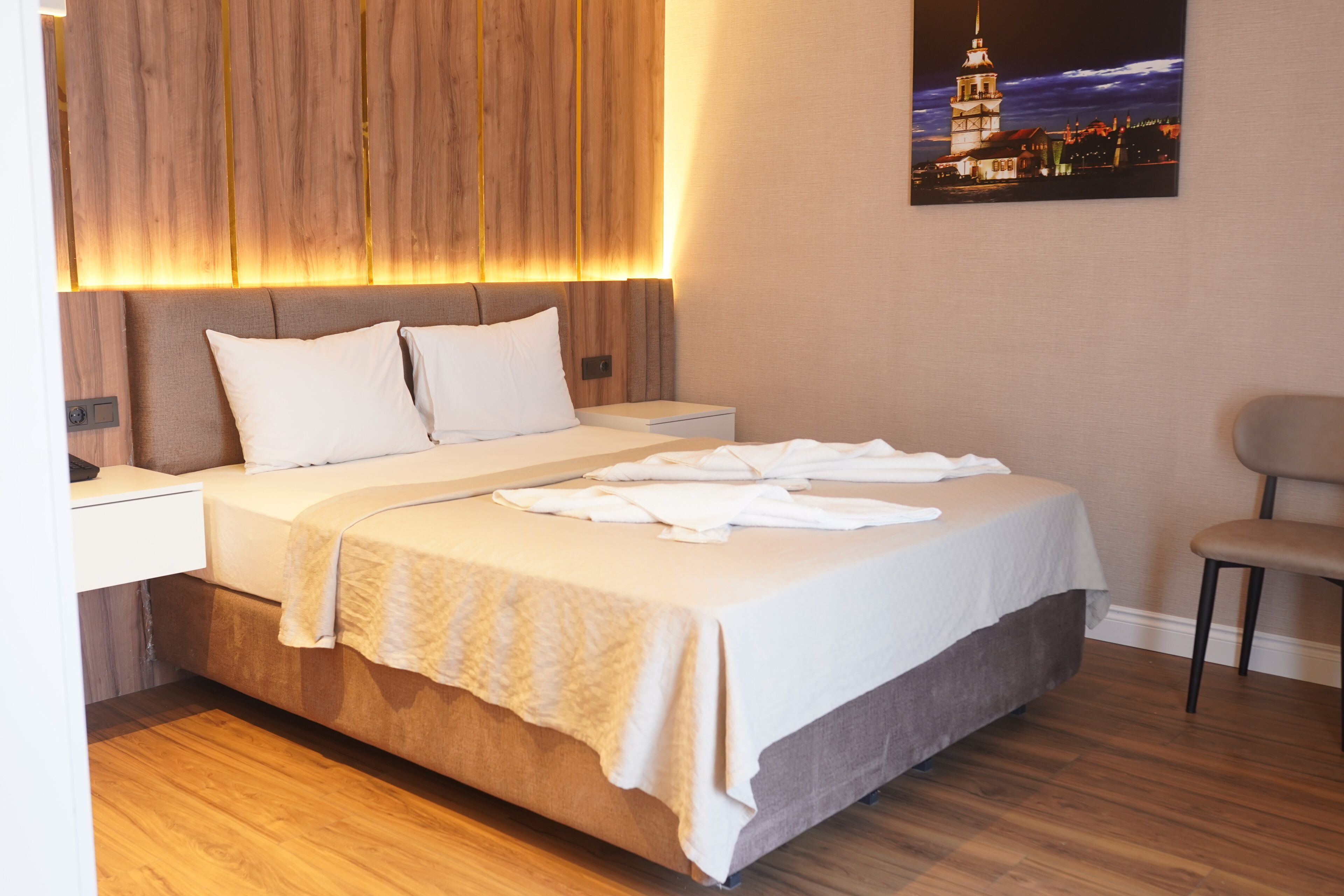 A hotel room with a wooden headboard, a bed with white linens, a bedside table, and a chair.