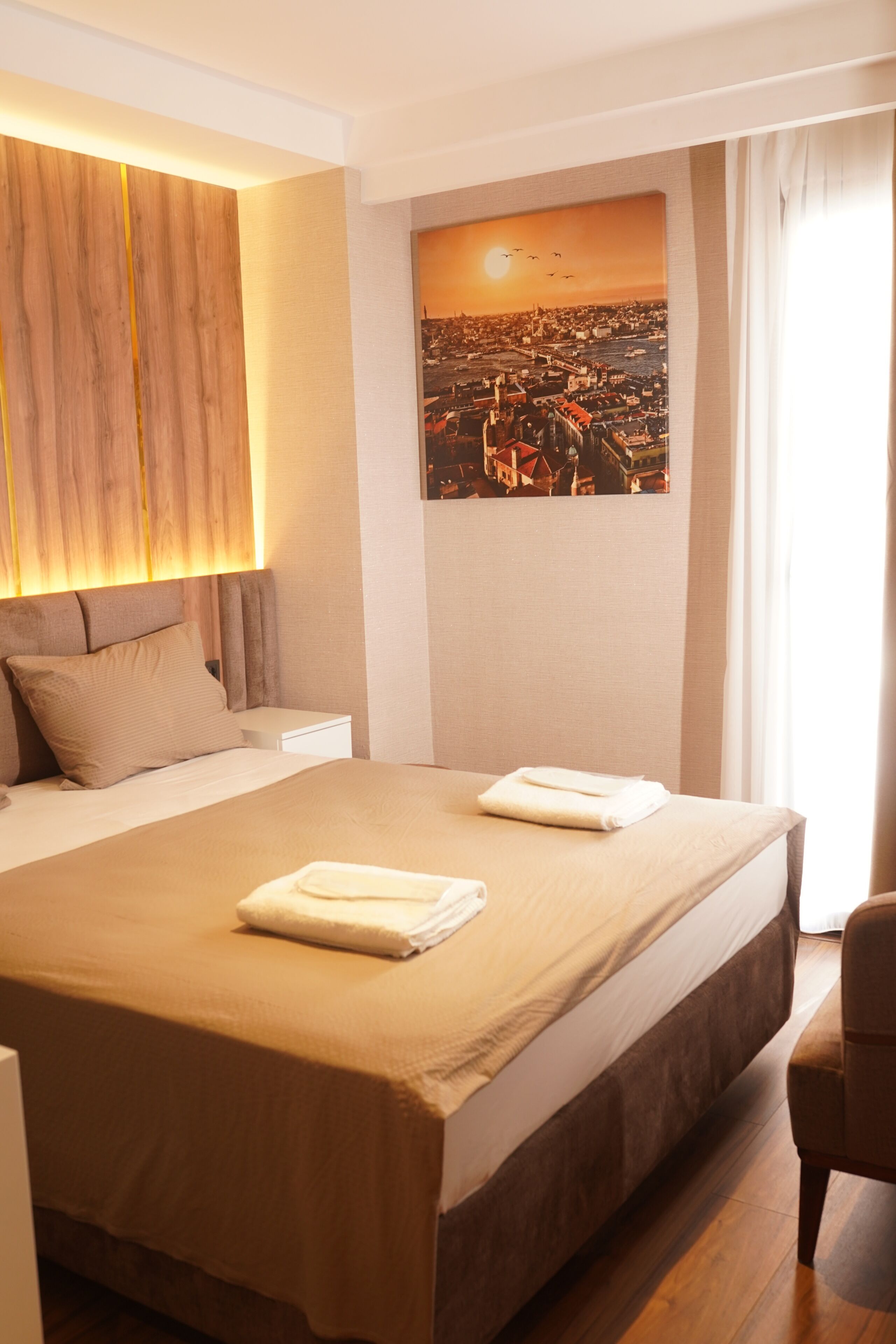 Habitación de hotel con una cama grande, una mesita de noche, una silla y vistas a la ciudad.
