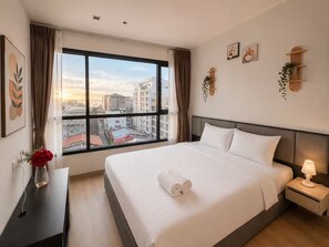 Ein Hotelzimmer mit einem großen Bett, einem Nachttisch mit Lampe, einem Fenster mit Vorhängen und Kunstwerken an den Wänden.