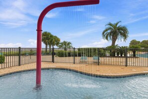 Ein Swimmingpool mit einer roten Wasserattraktion, umgeben von einem Zaun und Palmen.