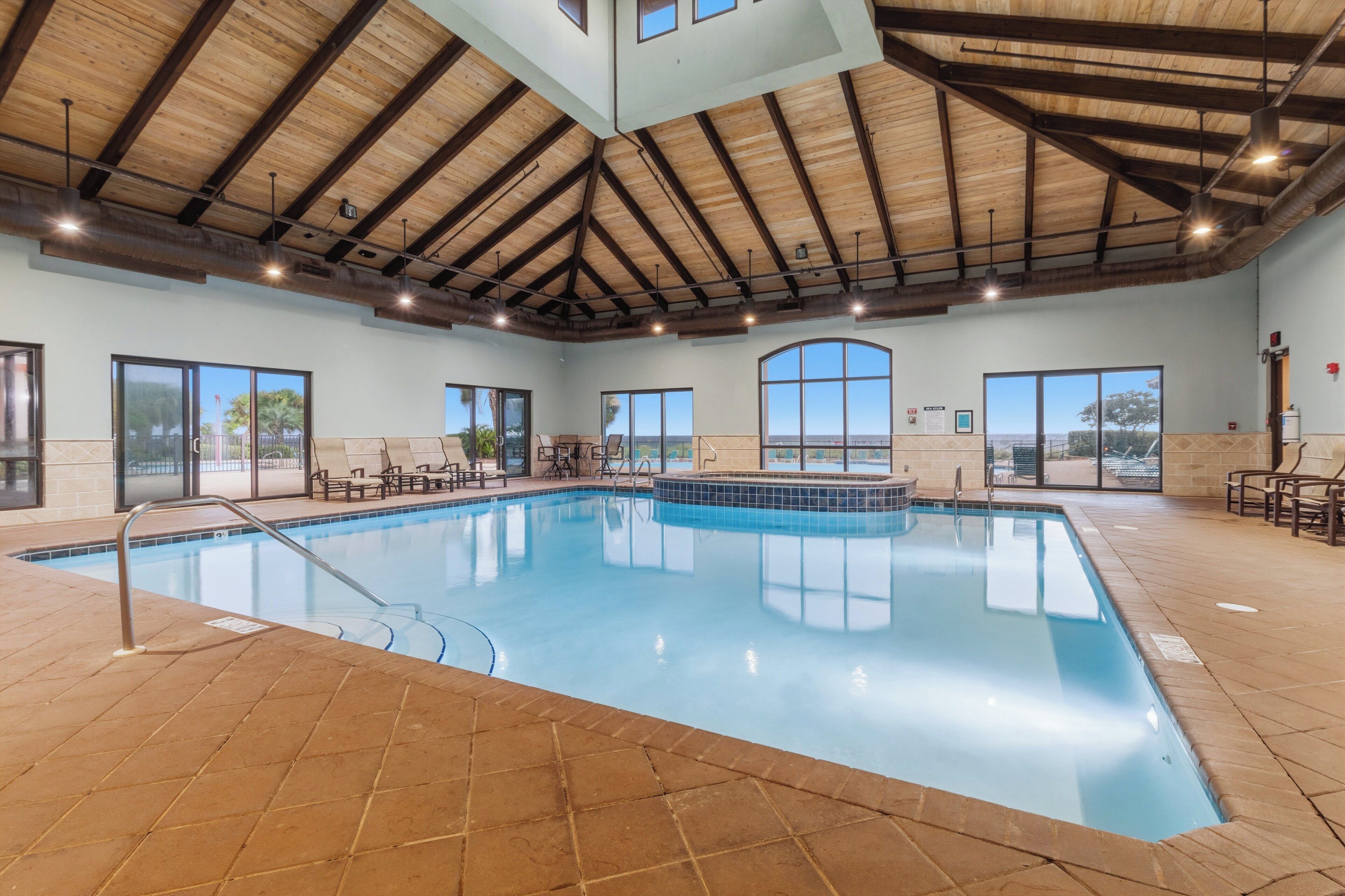 Une piscine intérieure avec un sol carrelé, de grandes fenêtres et un plafond en bois.