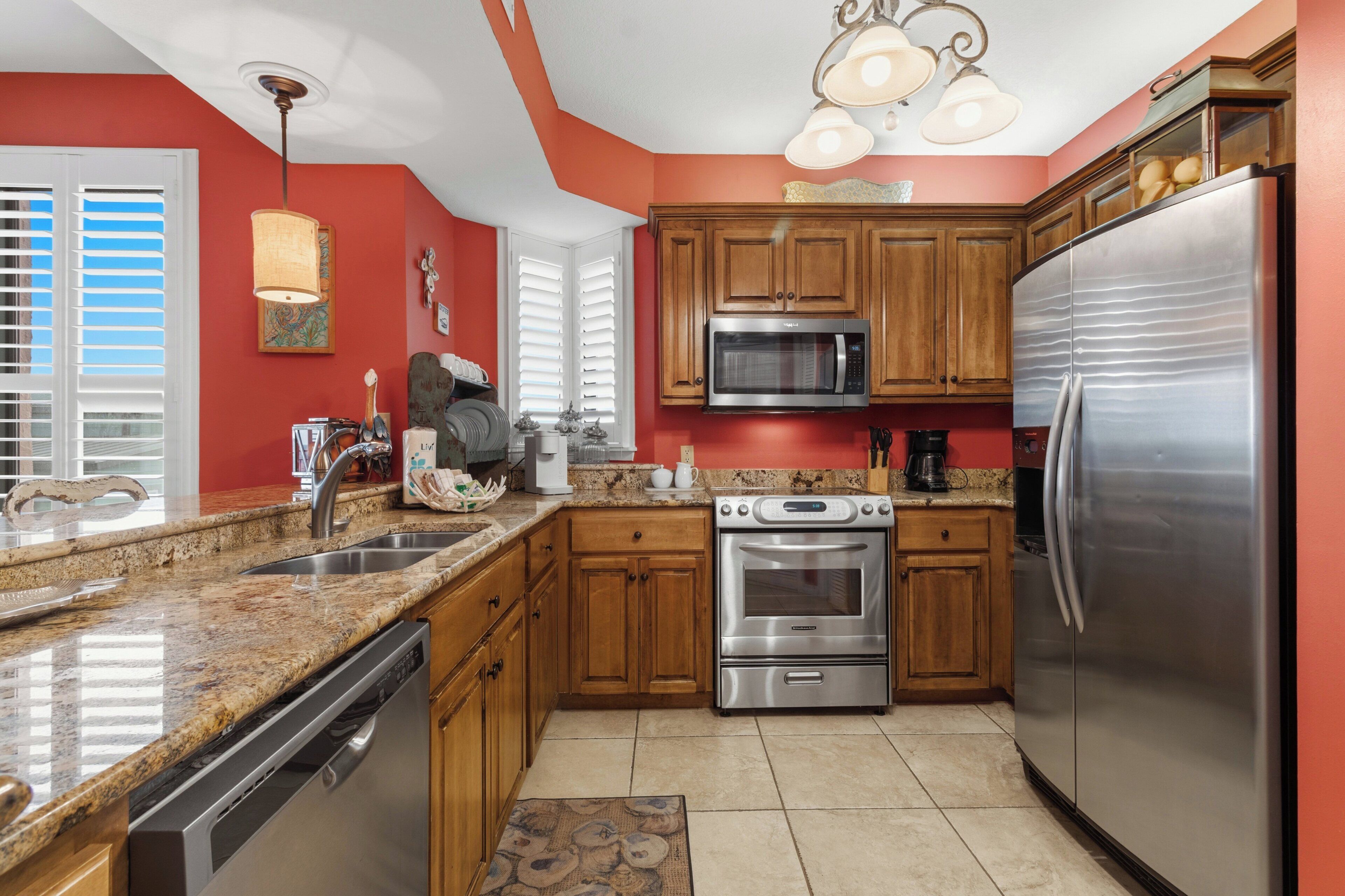 A kitchen with wooden cabinets, stainless steel appliances, a granite countertop, and a red accent wall.