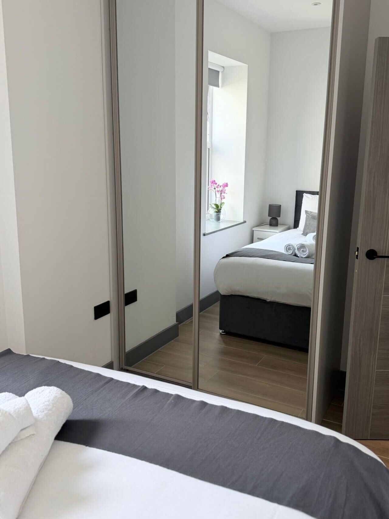 Une chambre à coucher moderne avec un lit, une table de chevet, une lampe et une fenêtre décorée de fleurs.