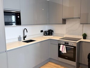 A modern kitchen with grey cabinets, a Bosch microwave, a sink, a coffee maker, and an oven. - Modern 2BR Flat | North Finchley (Greater London)