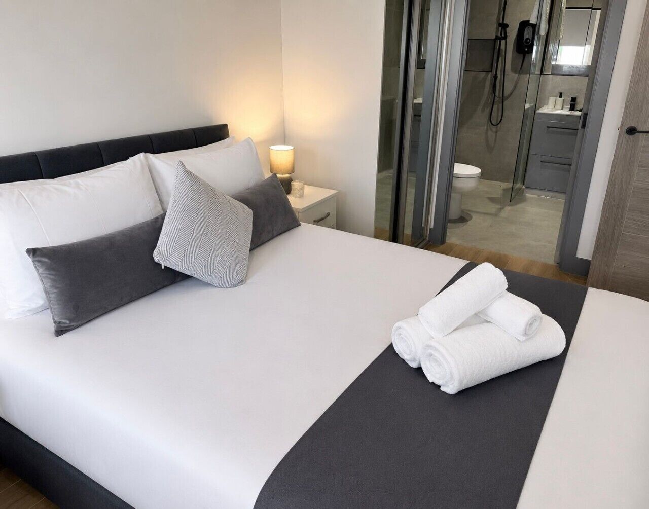 Une chambre d’hôtel avec un lit, des oreillers, une table de chevet avec une lampe et une vue sur la salle de bain.