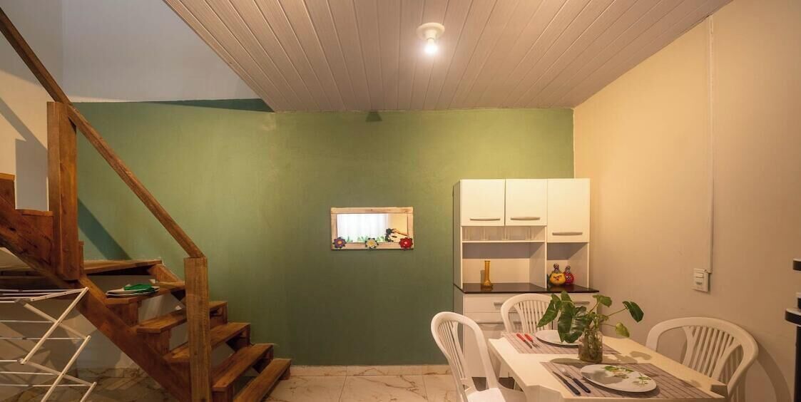 Un coin repas avec une table dressée pour deux personnes, un escalier en bois et une petite fenêtre donnant sur l’extérieur.
