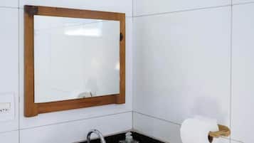 Ein Badezimmer mit weißen Fliesen, einem spiegel mit Holzrahmen, einem Waschbecken mit Armatur und einem Toilettenpapierhalter.