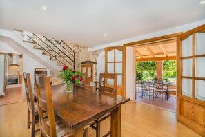 A dining area with a wooden table and chairs, a vase with flowers, a staircase, and a view of an outdoor patio. - Caseta DE Lloseta Ref Vp22 1 (Lloseta)