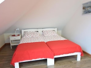 A single-bed room with a white headboard, a red blanket, a bedside table with a lamp, and a small drawer.