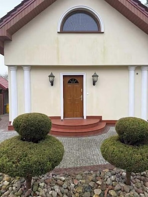 A building with a symmetrical facade, a central entrance with a door, and two symmetrical shrubbery on either side.