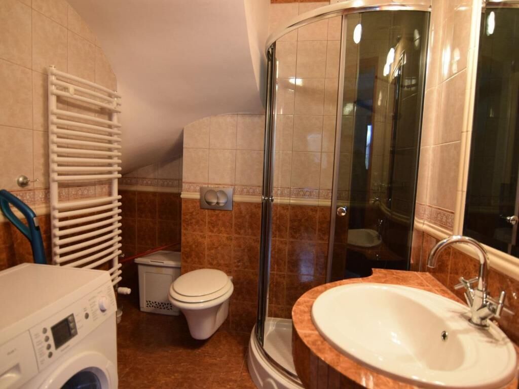 A bathroom with a glass shower enclosure, a white sink, and a washing machine.