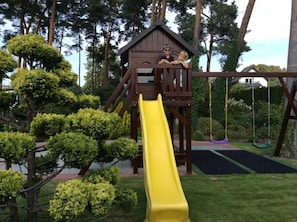 A playground with a yellow slide, a wooden climbing structure, and a swing set.