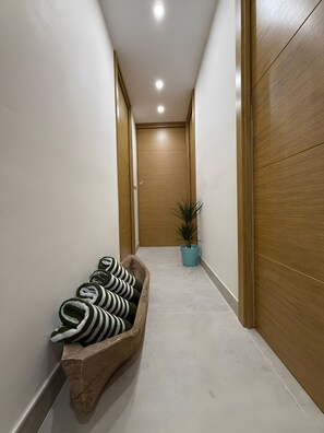 A hallway with a wooden door at the end, a potted plant, and a wooden bench with rolled-up mats.