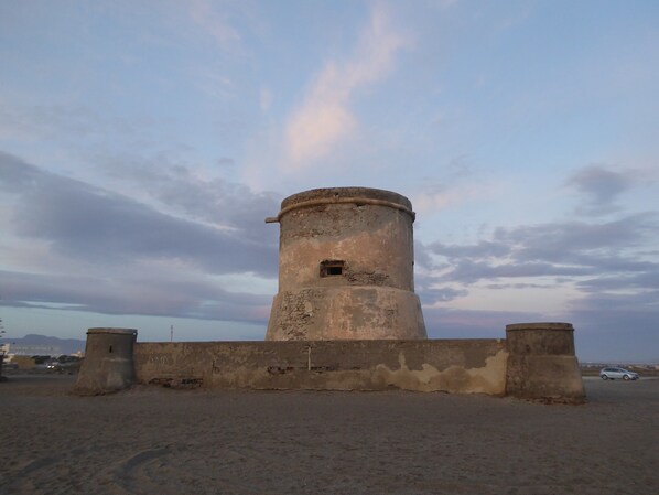 Una torre cilíndrica con una pequeña ventana, rodeada por un muro bajo, frente a un cielo nublado.