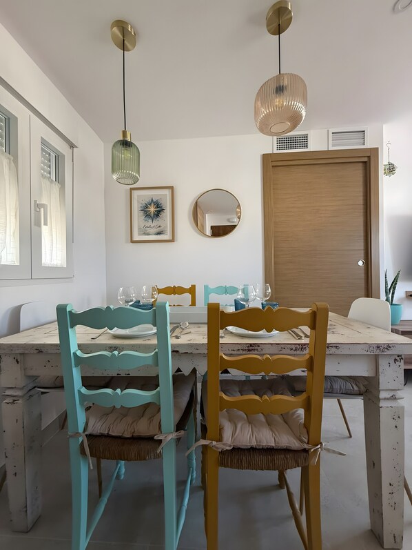 A dining area with a white table, teal and yellow chairs, and pendant lights.