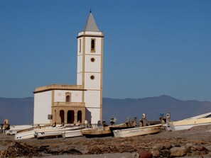 Una iglesia con un campanario y un reloj, rodeada de barcos en una orilla arenosa.