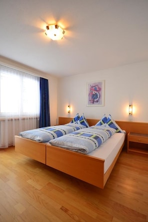Ein Schlafzimmer mit einem hölzernen Bett, zwei Nachttischlampen, einem Fenster mit Vorhängen und einem an der Wand befestigten Kunstwerk.