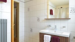 Een badkamer met een witte betegelde vloer, een houten wastafelmeubel met spiegel en twee handdoeken aan de wand.