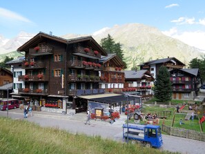 Ein mehrstöckiges Hotel mit Balkonen, die mit Blumen geschmückt sind, ein Restaurant und ein Spielplatz.