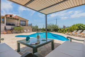 A poolside area with a glass table, lounge chairs, and a building in the background. - 6-guest Stone Haven in Pollensa (Pollença)