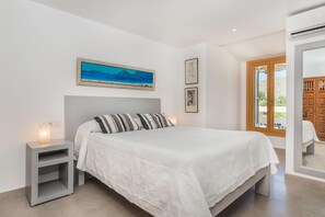 A bedroom with a bed, bedside tables, a painting, and a door leading to an outdoor area. - 6-guest Stone Haven in Pollensa (Pollença)