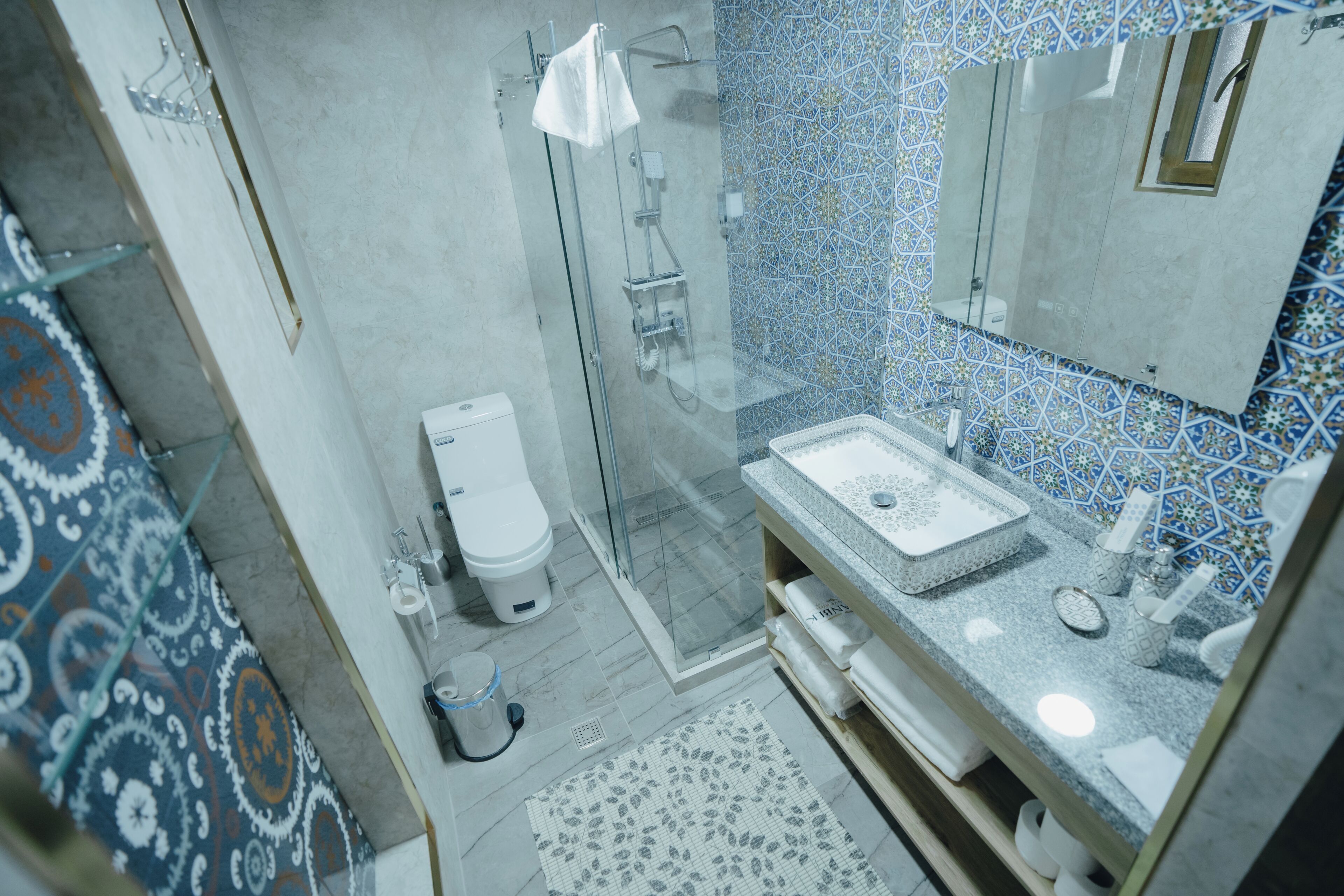 A bathroom with a glass shower enclosure, a white toilet, and a sink with a patterned countertop.