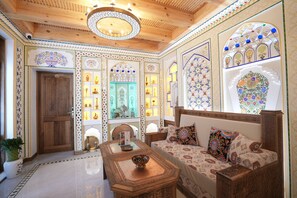 A traditional interior with a wooden ceiling, ornate wall decorations, and a seating area with cushions. - Imranbek Boutique Hotel (Bukhara)