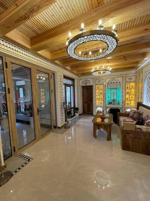 A spacious room with a wooden ceiling, a chandelier, and a seating area with a coffee table. - Imranbek Boutique Hotel (Bukhara)