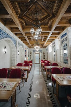 A long corridor with tables and chairs, wooden ceiling beams, and patterned walls. - Imranbek Boutique Hotel (Bukhara)