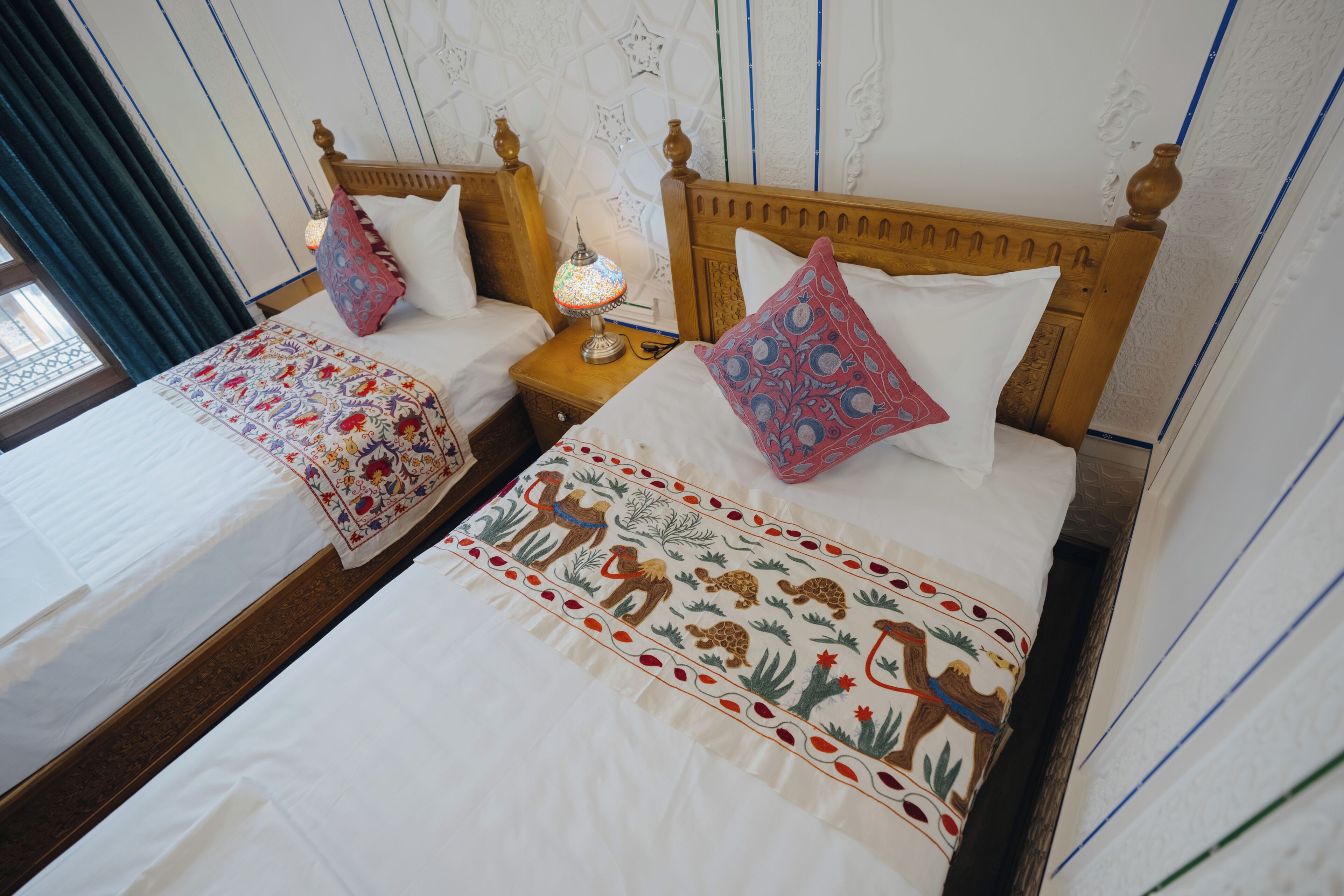 Habitación de hotel con dos camas individuales, cada una con cabecero de madera, mesita de noche y lámpara.