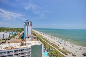 A coastal hotel with a prominent tower, a beach with umbrellas, and a clear view of the ocean. - Ocean View 1BR Suite + Beach Access + Lazy River (Myrtle Beach)