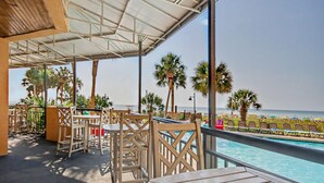 A poolside area with a view of the ocean, wooden furniture, and a covered seating area.