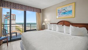 A hotel room with a large bed, a balcony with a view of the city, and a painting on the wall.