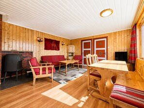 Une pièce chaleureuse avec un plafond en bois, un canapé rouge, une table à manger en bois et un téléviseur.