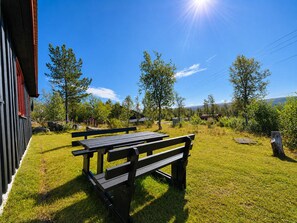 Un banc en bois, situé dans un espace verdoyant, avec un bâtiment en arrière-plan.