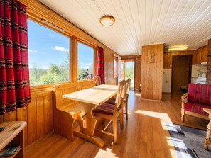 Un intérieur en bois comprenant une table et des chaises de salle à manger, un coin cuisine et de grandes fenêtres avec des rideaux.