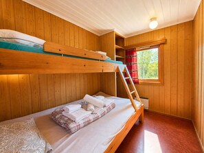 Ein Schlafraum mit Etagenbetten, Holzwänden, einem Fenster mit roten Vorhängen und einer Klapptreppe.